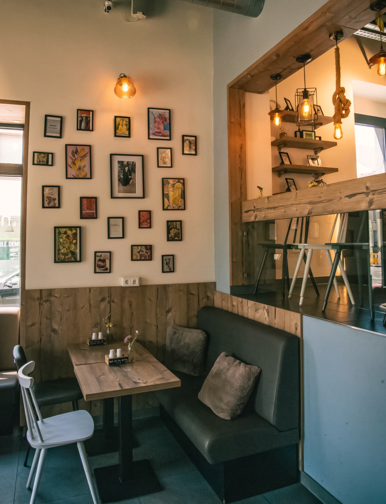 Sitzecke mit Holztisch, gepolsterter Bank, Bilderwand und warmen Pendelleuchten.