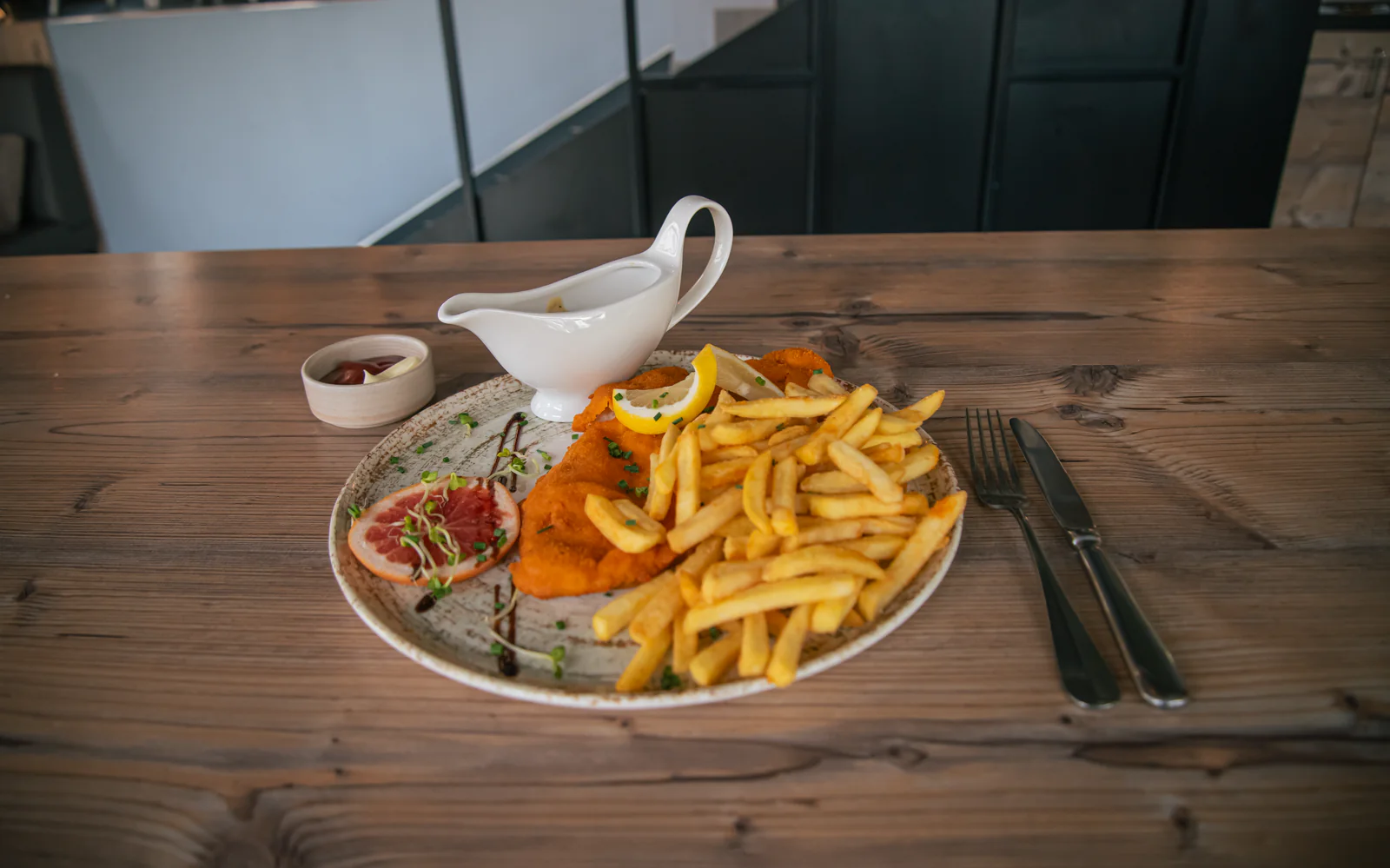 Paniertes Schnitzel mit Pommes, Zitronenspalten und Soße.
